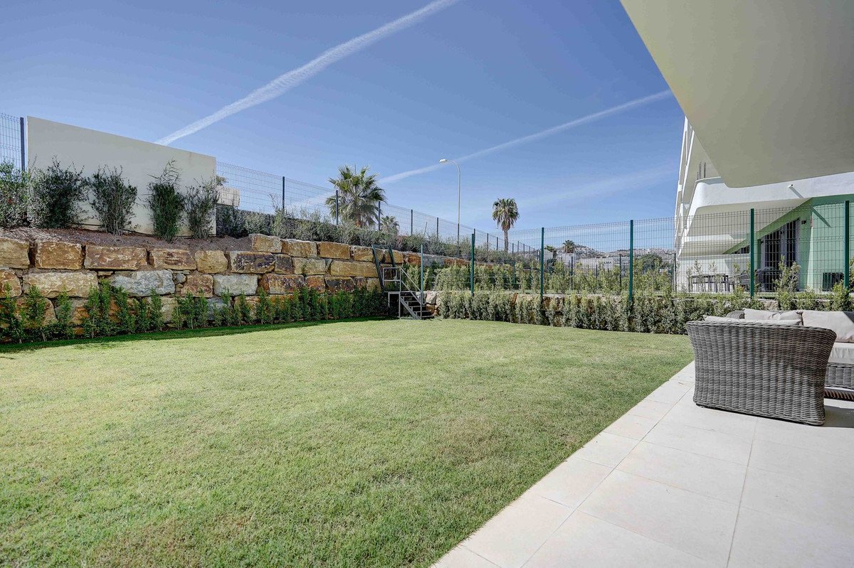 A spacious private garden with a well-maintained lawn, stone retaining wall, and a patio area with outdoor seating.