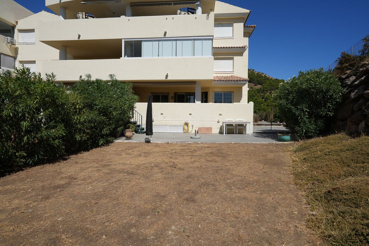 Exterior of a building showing a terrace with an umbrella and garden area in front.