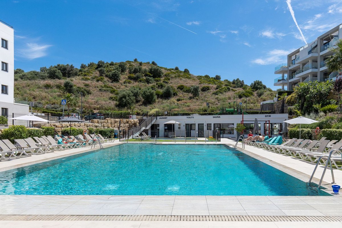 A spacious outdoor swimming pool with lounge chairs and a building offering laundry, toilets, sauna, and gym facilities.