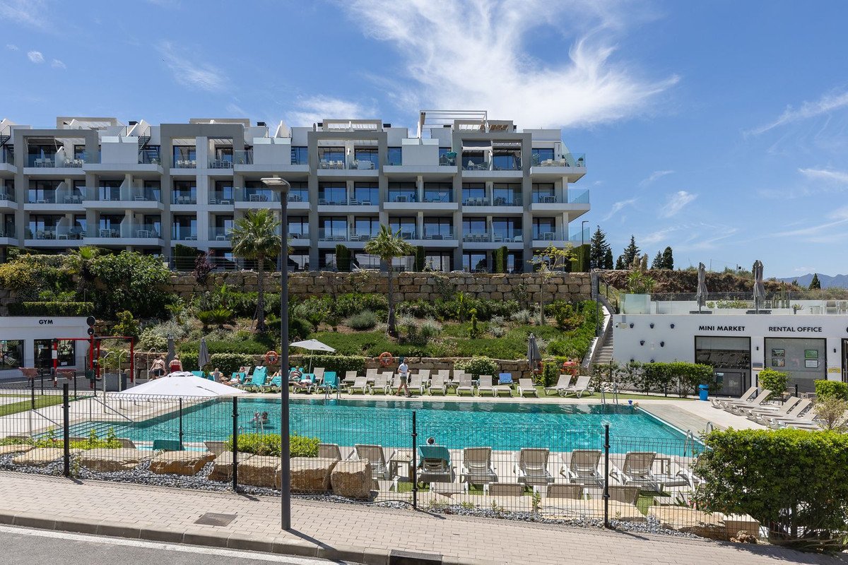 Modern apartment complex with a swimming pool, sun loungers, gym, and mini-market on a sunny day.