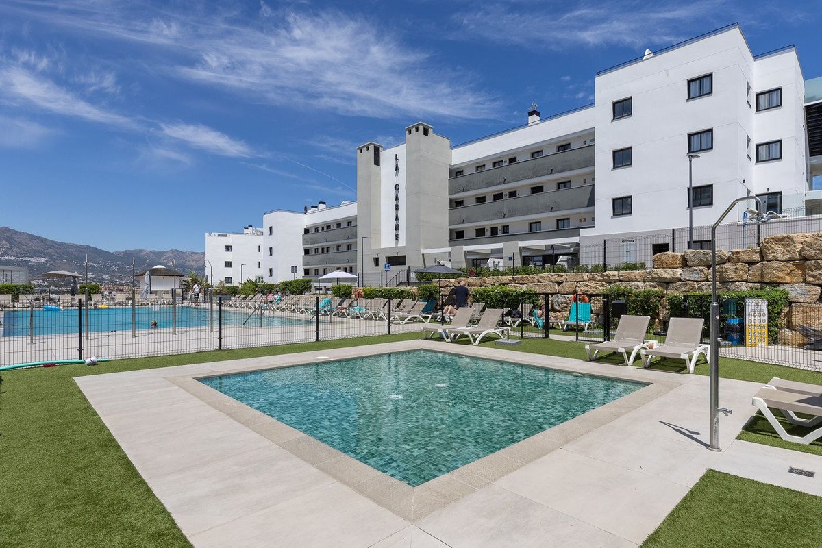 Modern resort complex with swimming pools, lounge chairs, and mountain views under a clear blue sky.