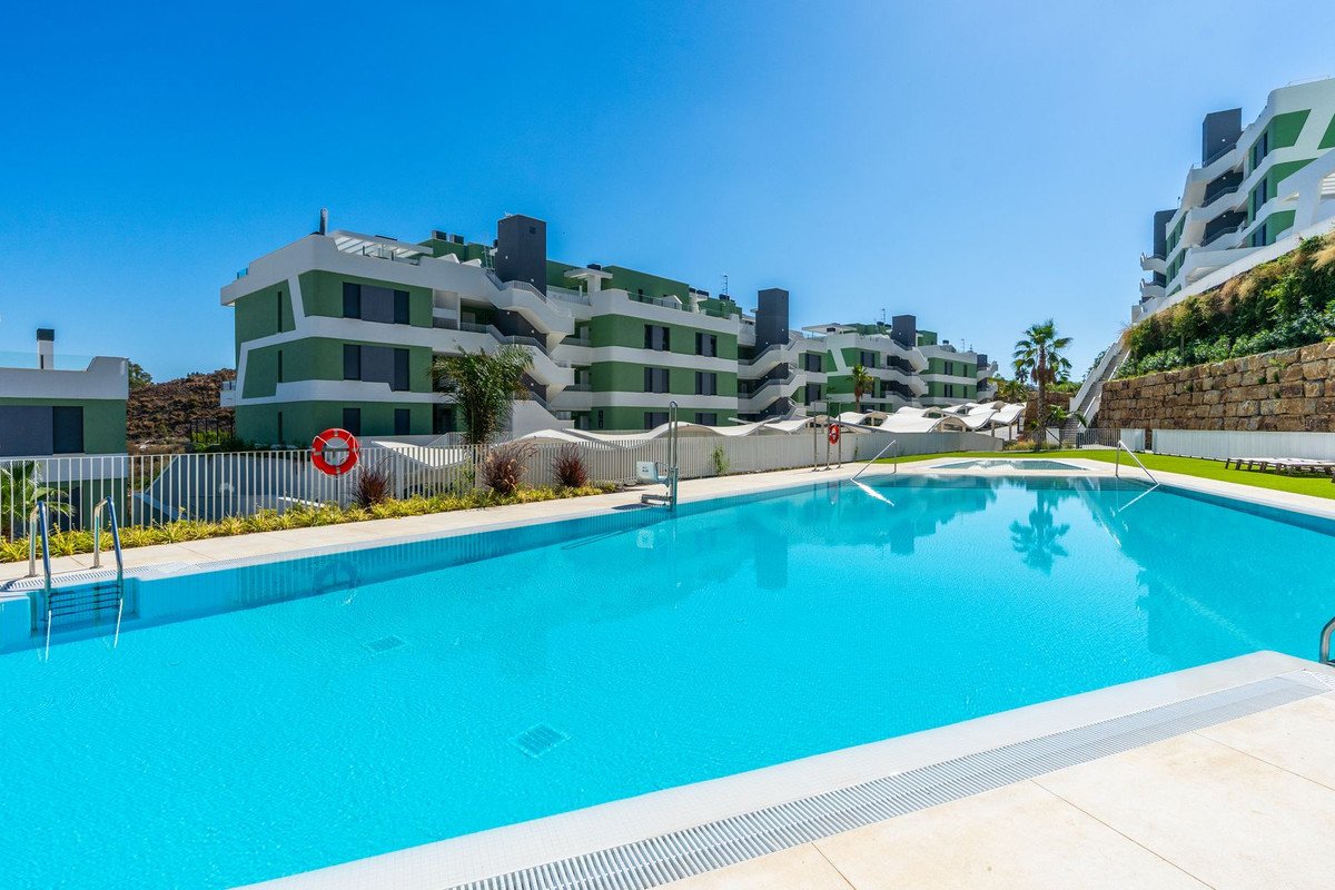 A large bright blue swimming pool in front of modern apartment buildings with green and white facades, under a clear blue sky.