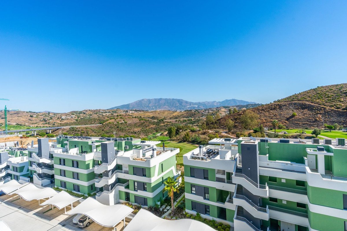 Modern apartments with green facade and balconies, offering mountain and golf course views under a clear blue sky.