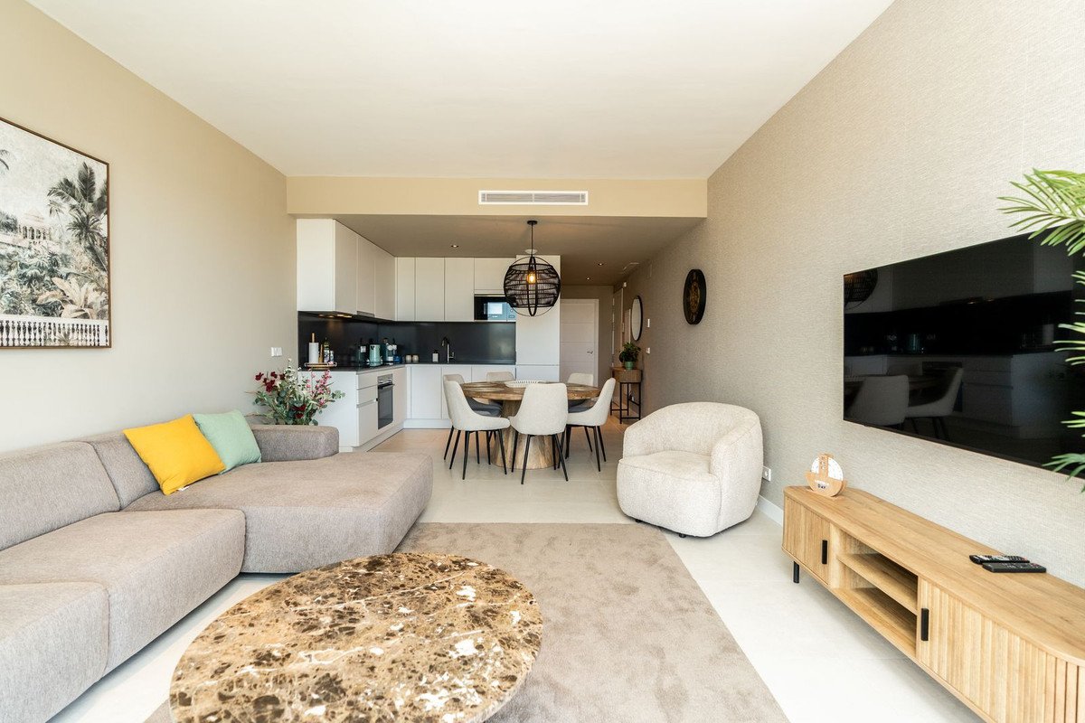 Modern open-plan living area with a sectional sofa, dining table, and kitchen. Features a TV and stylish decor.