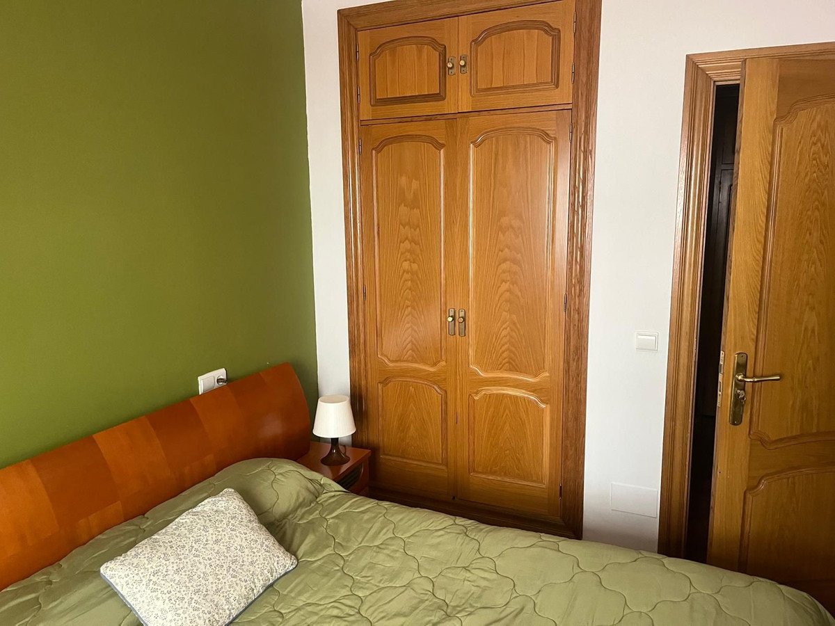 A bedroom with a green wall, wooden wardrobe, and bed with green bedding.