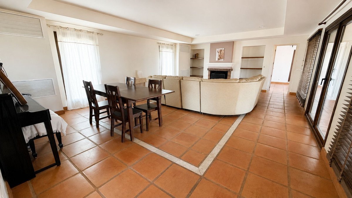Spacious living and dining area with a curved sofa, fireplace, dining table, chairs, and a piano.