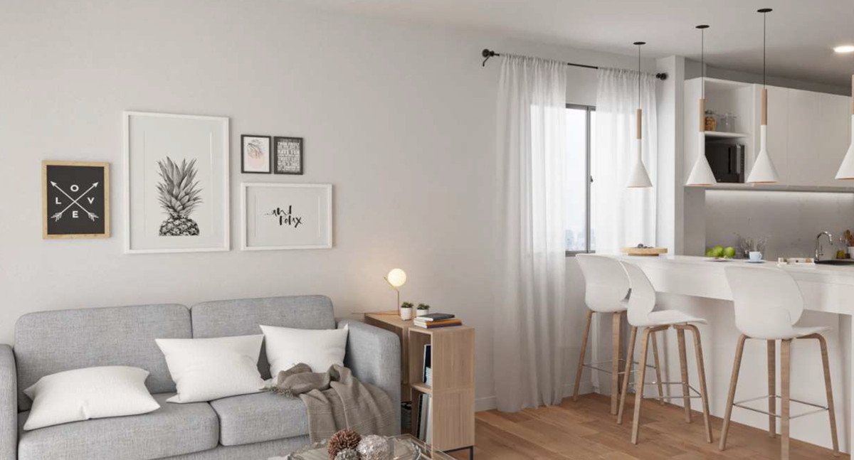 A modern living room area with a grey sofa and a kitchen island with white bar stools, featuring artwork and pendant lights.