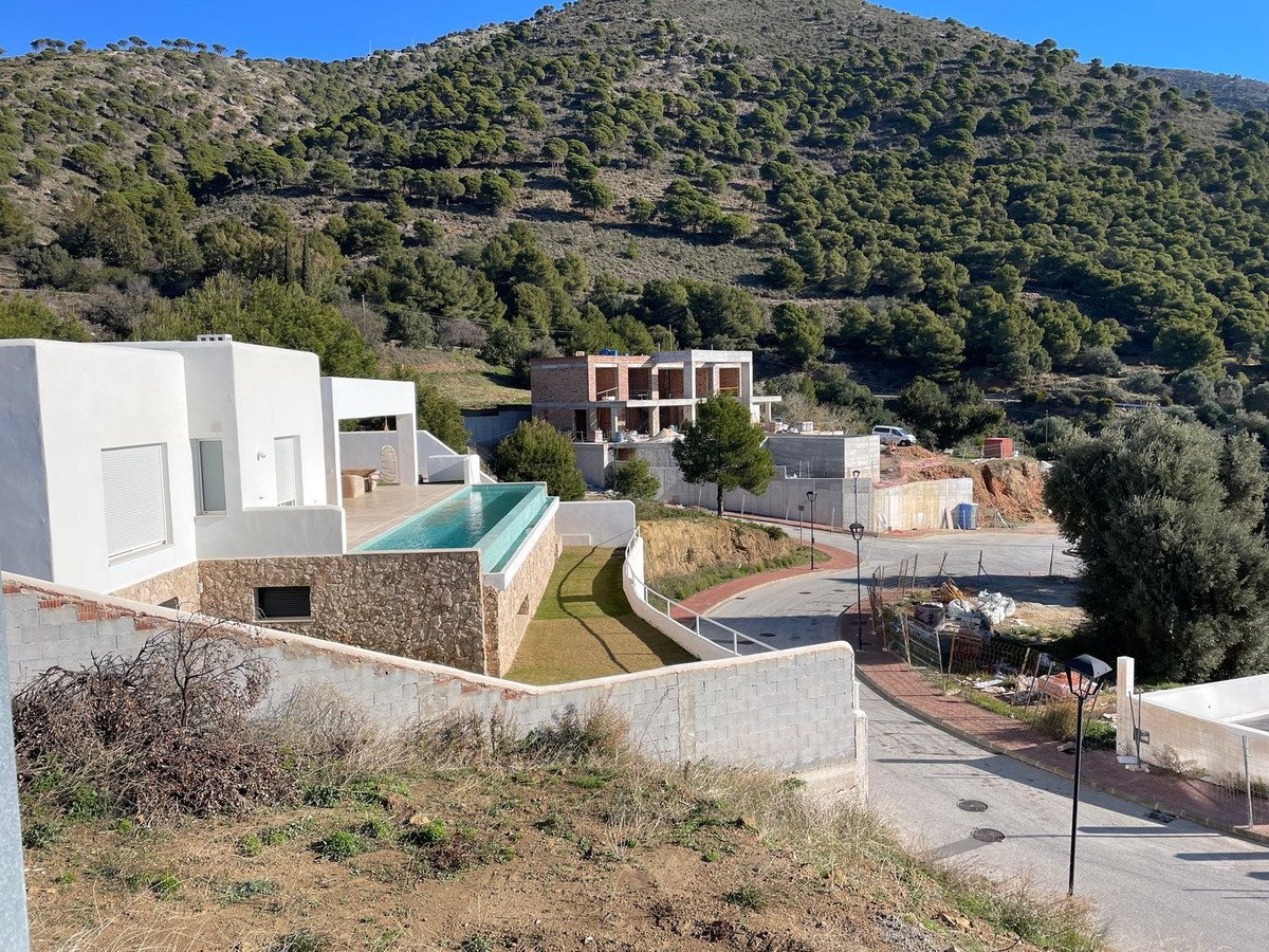 Modern villa with infinity pool overlooking a forested hillside under a clear blue sky.