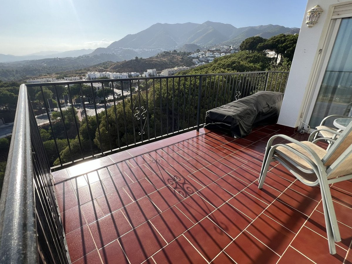 Terrace with chairs and a covered lounger overlooking a valley and mountains in the distance.