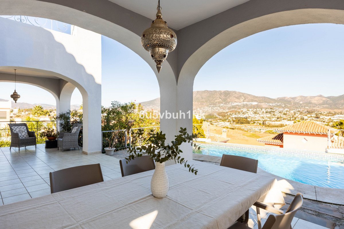 Covered patio with dining table and chairs, overlooking a pool and scenic mountain landscape.