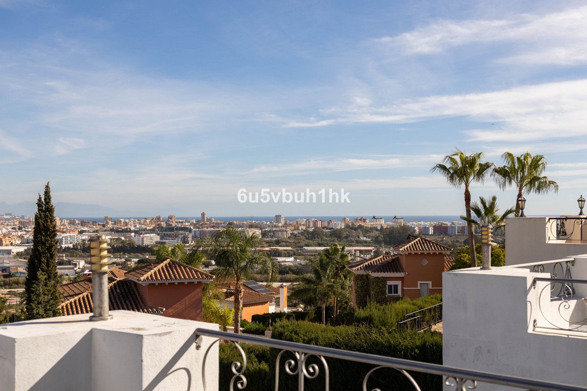 A wide view from a terrace overlooking a city and the sea, with palm trees and rooftops visible.