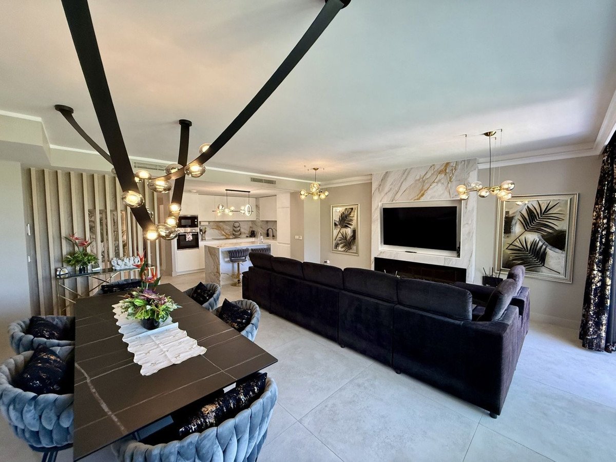 A spacious open-plan living, dining, and kitchen area with modern furniture, a large sofa, and a marble fireplace with a TV.