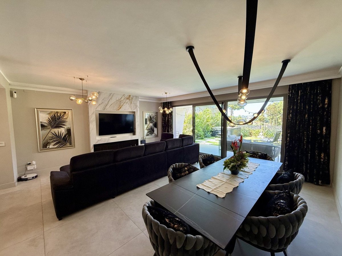 Modern living and dining room with large windows overlooking a lush green garden and patio furniture.
