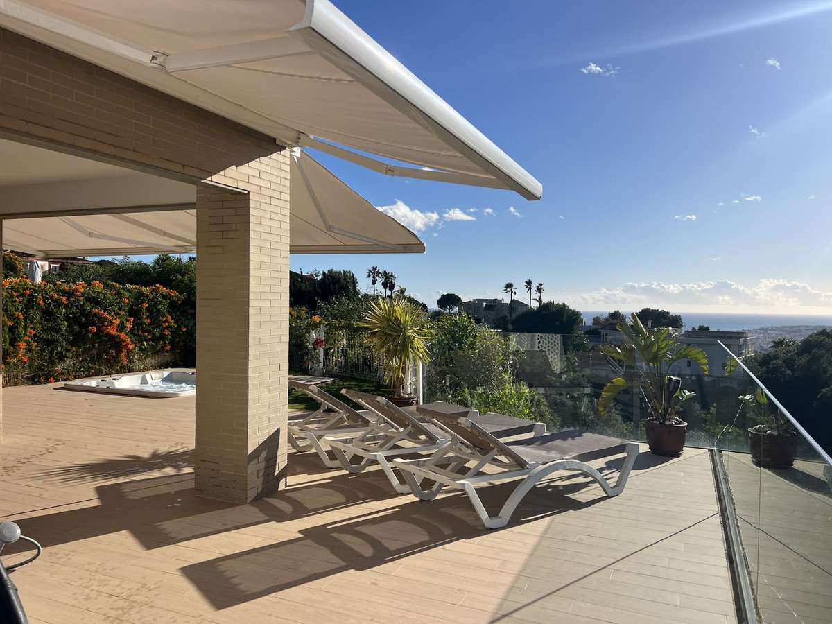 Covered terrace with sunbeds and a hot tub, overlooking a distant sea view under a sunny blue sky.