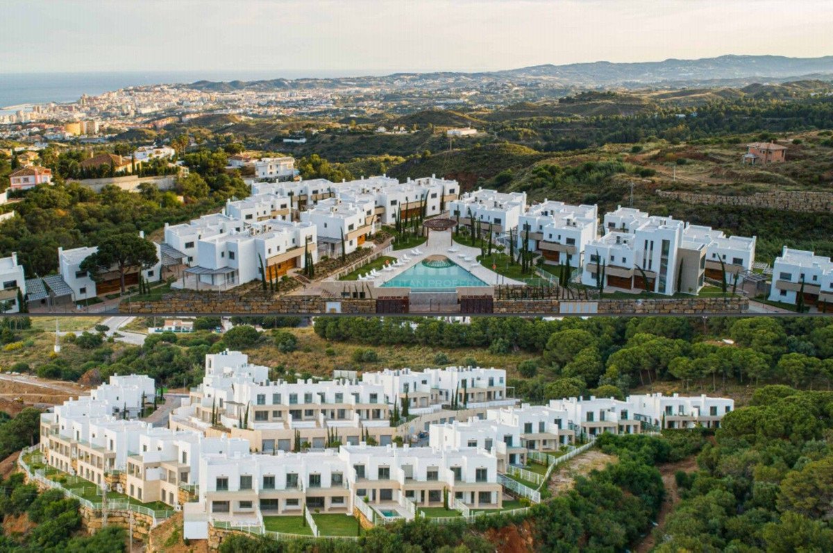 Aerial view of a modern resort community with white buildings, a large swimming pool, and distant sea and city views.