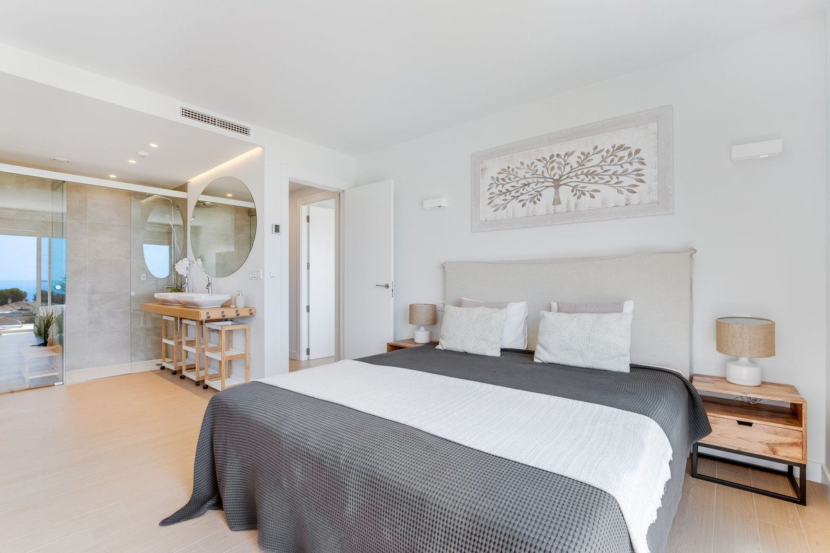 A spacious master bedroom with a large bed, ensuite bathroom, and large windows offering a view of the sea.