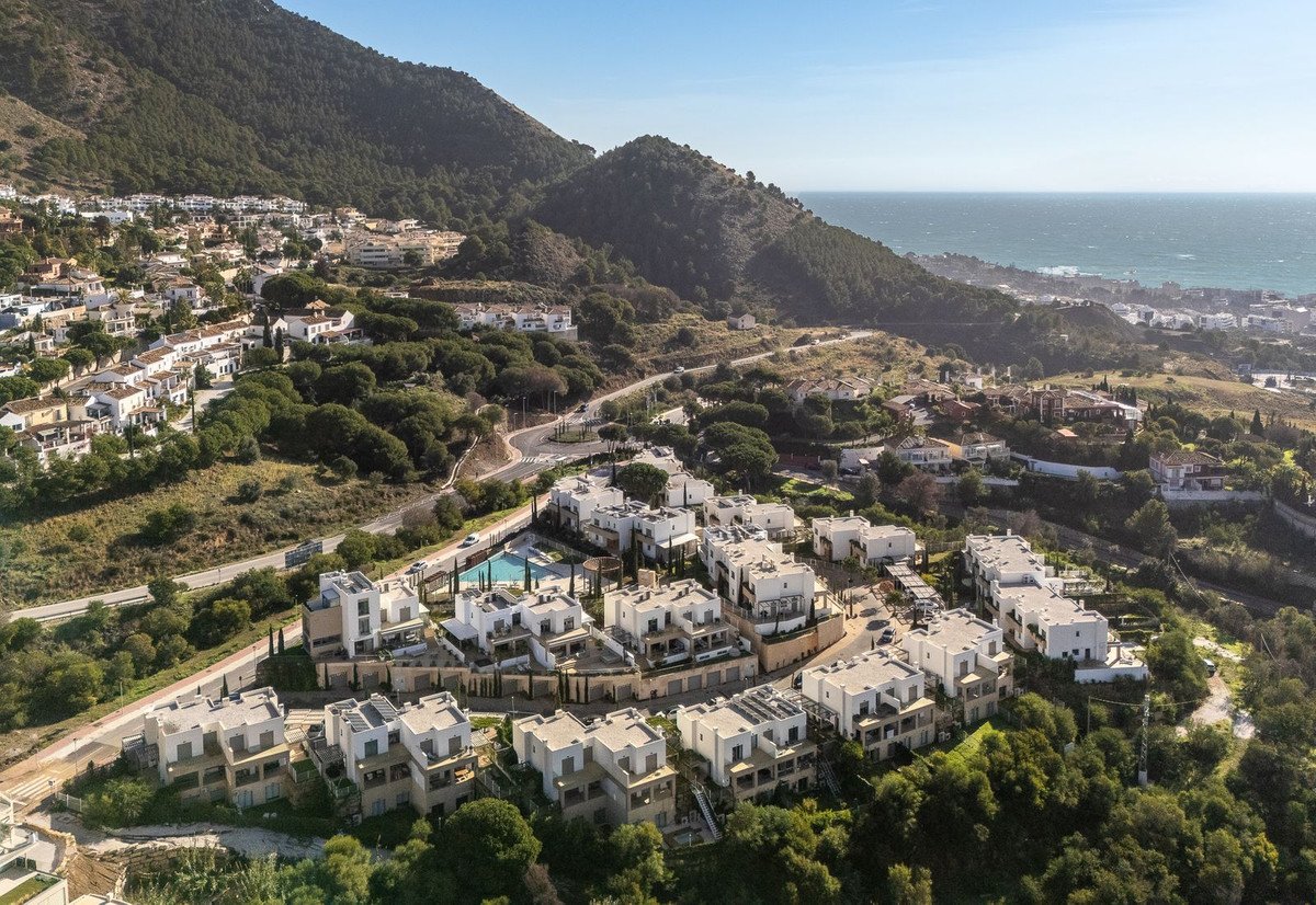 Aerial view of a modern villa complex nestled on a hillside with a pool and overlooking the sea and distant town.