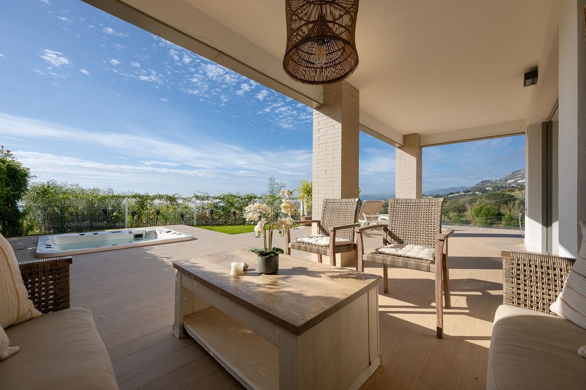Modern covered terrace with a hot tub, seating area, coffee table, and stunning sea and mountain views.