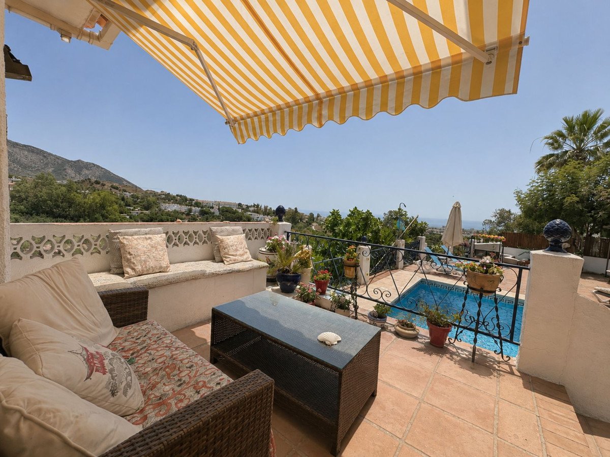 A sunny terrace with a pool and sea view, featuring comfortable seating and a retractable awning.