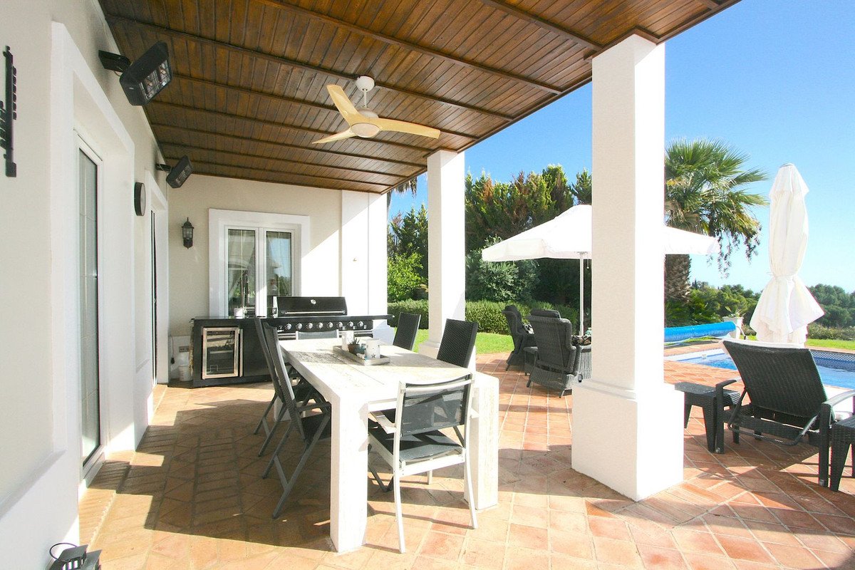 Covered patio with dining table, grill, chairs, umbrellas, and pool view.