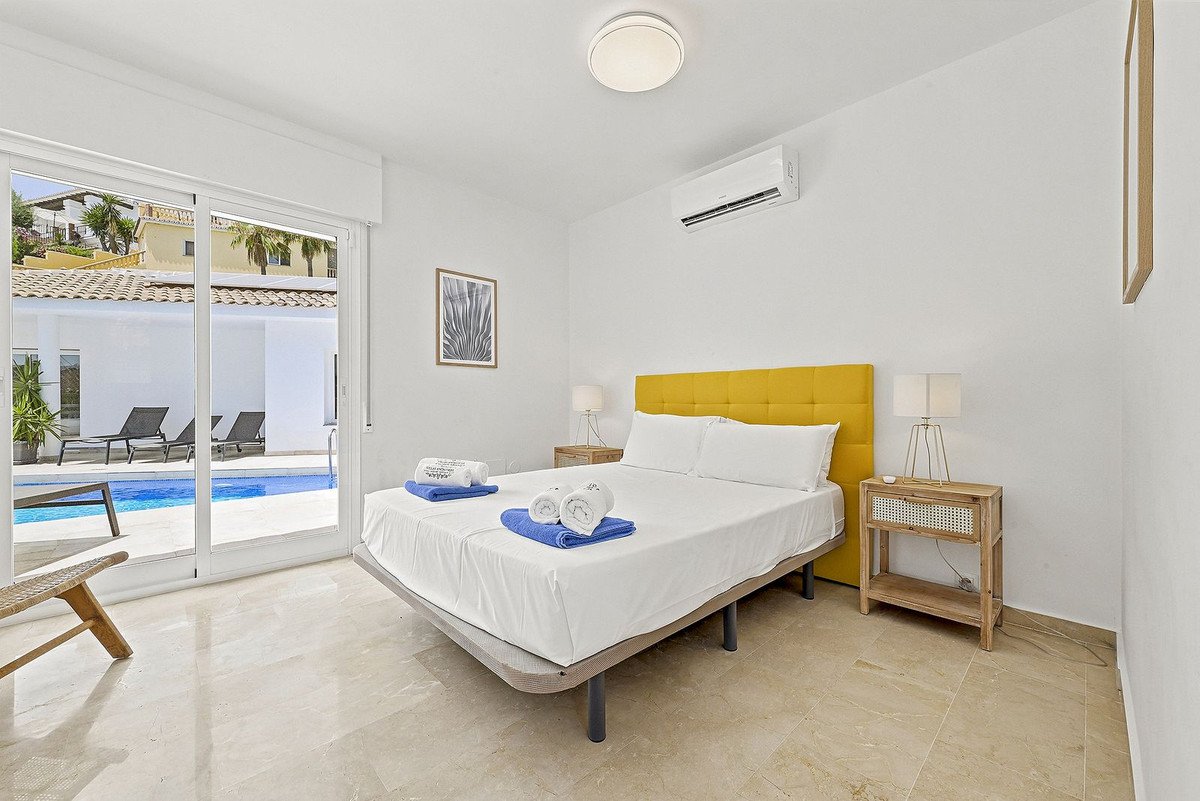 Modern bedroom with a double bed, yellow headboard, and sliding doors opening to a private swimming pool area with lounge chairs.