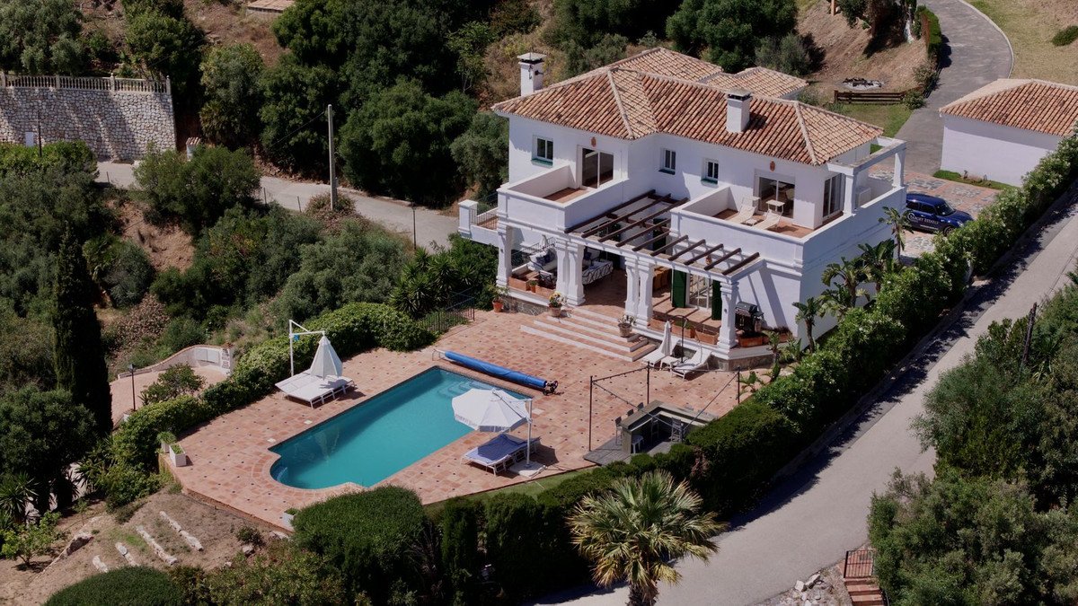 Aerial view of a white villa with terracotta roof, private pool, and lush green surroundings.