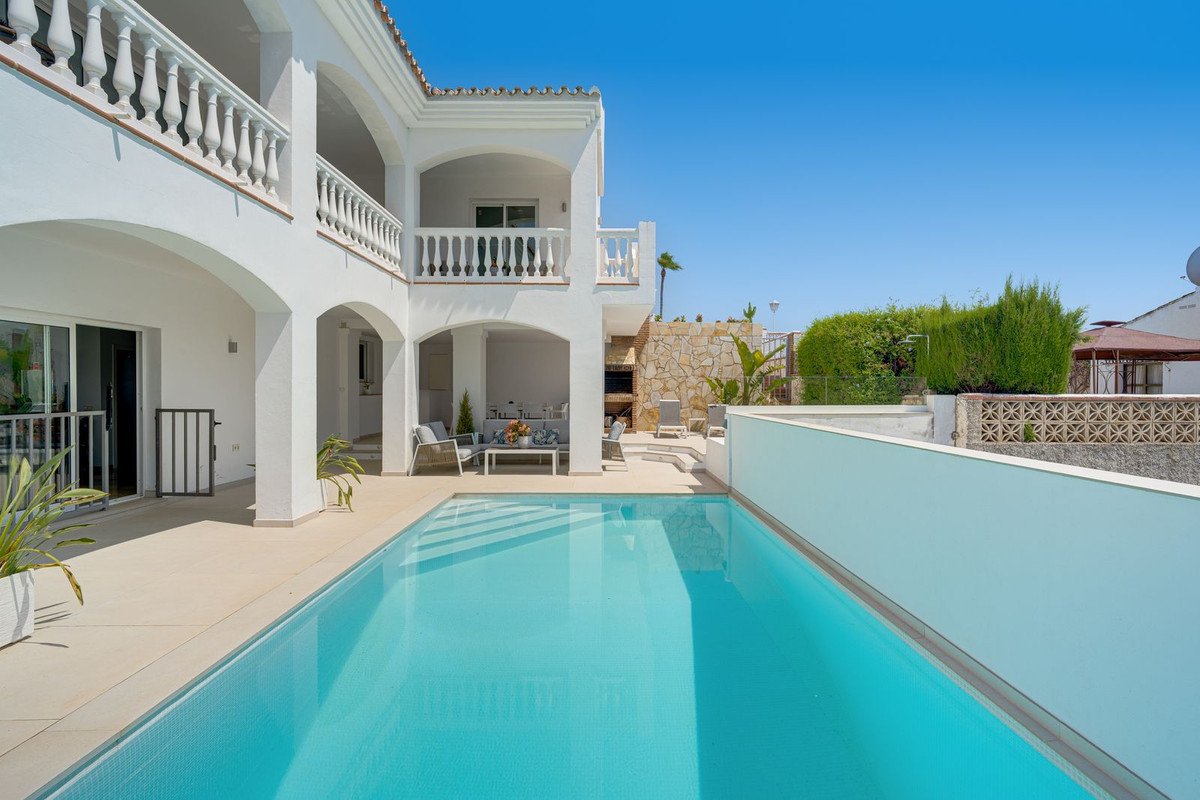 Swimming pool with white house and lounge chairs under clear blue sky