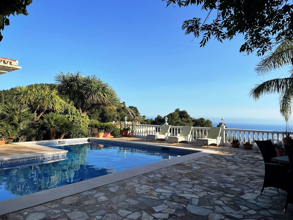 Villa with pool, sun loungers, and ocean view from stone patio.