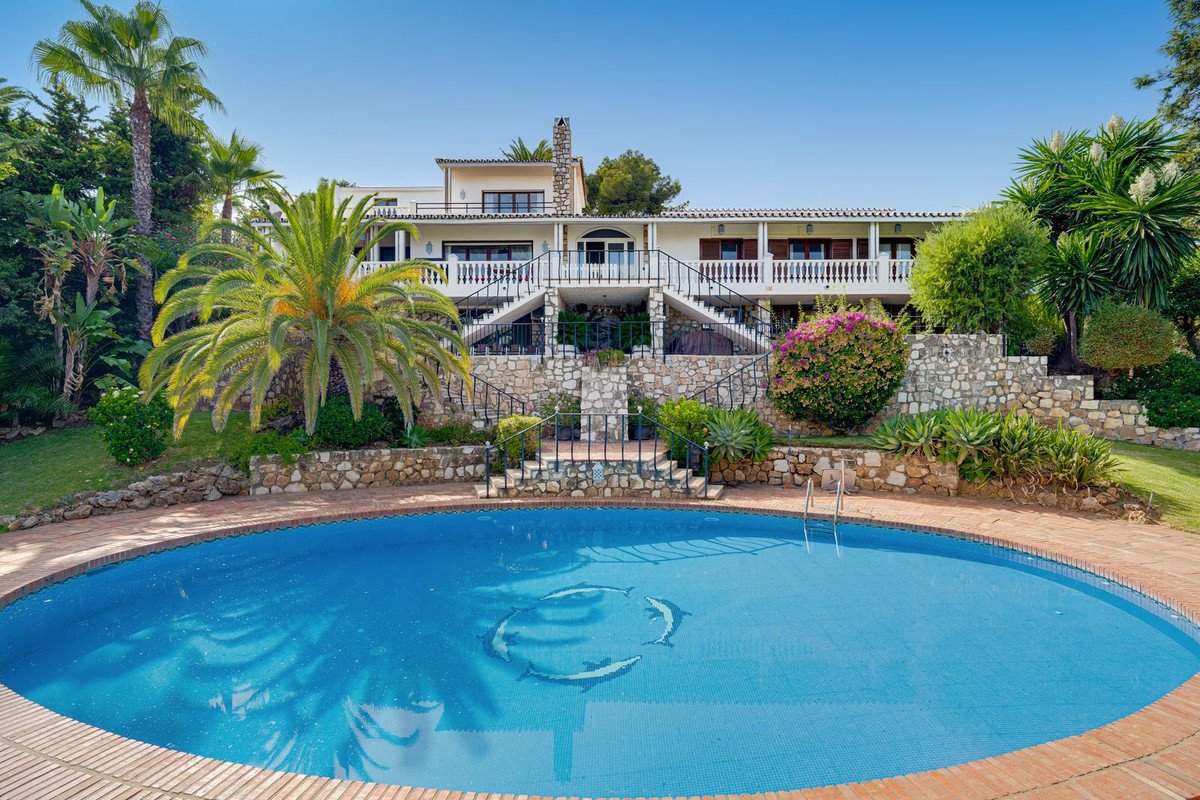 Luxury villa with a large oval swimming pool and palm trees, offering a picturesque view.