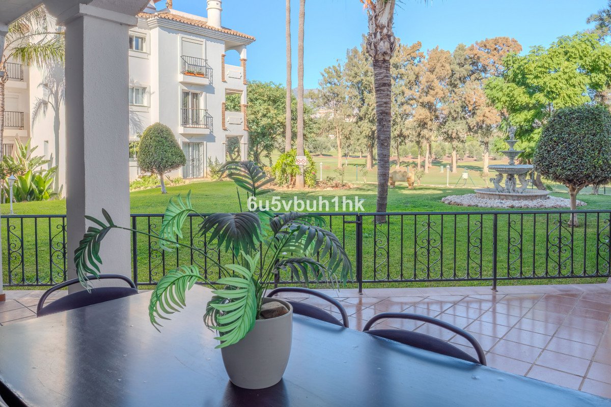 Terrace view of a manicured garden with a fountain, trees, and a residential building in the background.
