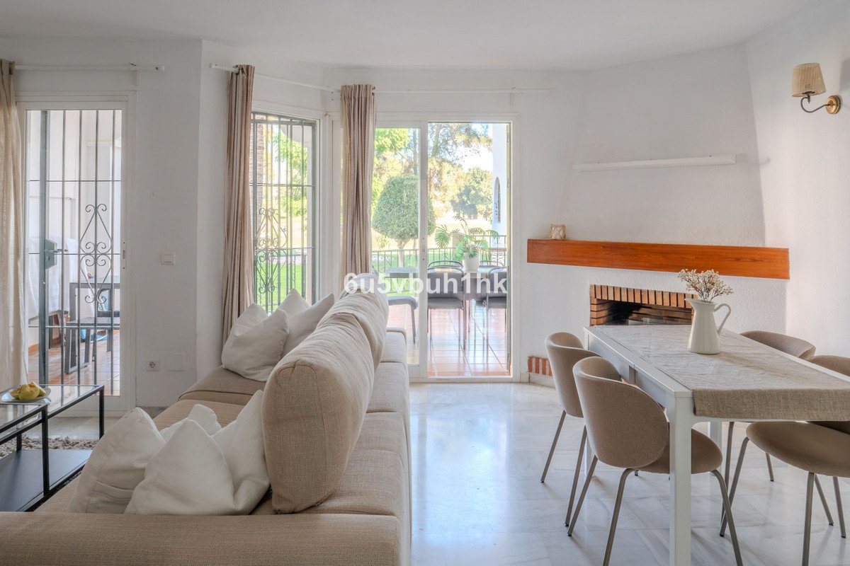 Bright living room with a large sofa, dining table, fireplace, and sliding doors opening to a garden terrace.