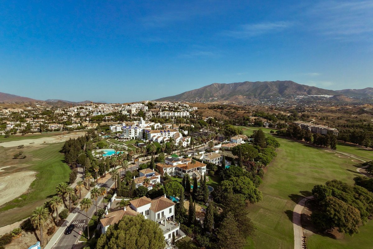Aerial view of luxury villas and resort buildings surrounding a golf course, with mountains in the background.
