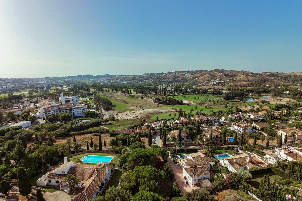 Aerial view of villas and golf course with swimming pools and lush greenery under a clear blue sky.