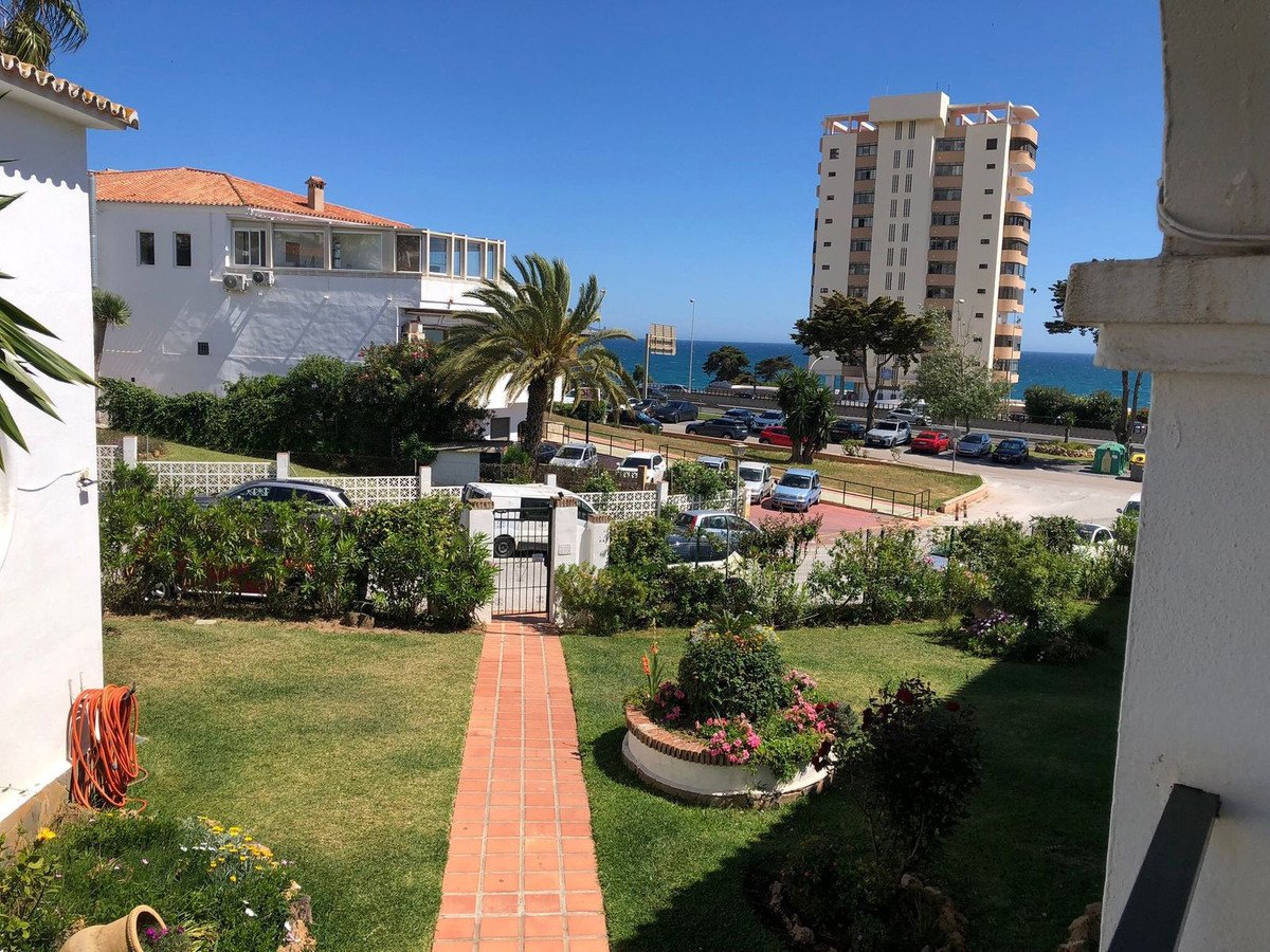 A brick path leads through a green garden towards a distant view of the sea and a tall building.