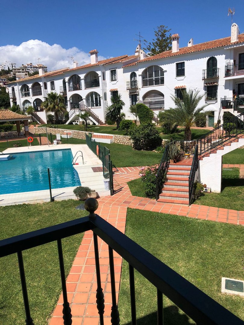 View of a swimming pool and residential buildings with white facades and red tile roofs on a sunny day.