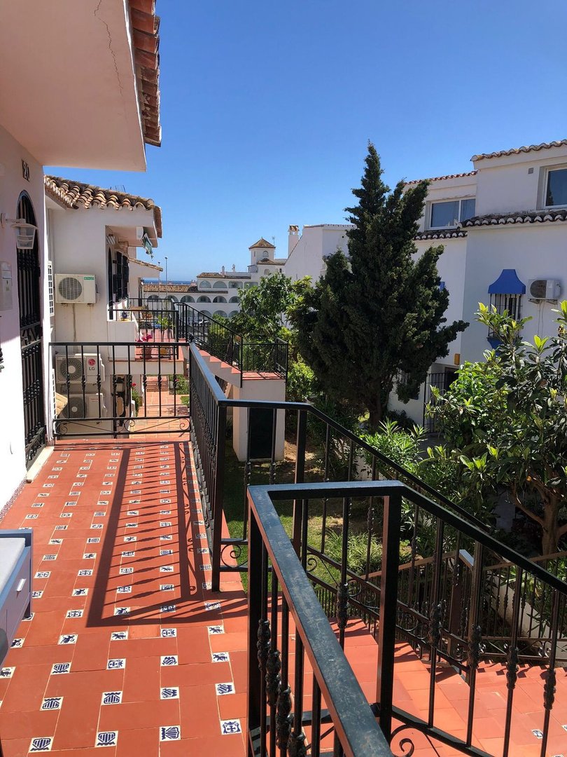 Sunny terrace with tiled floor and stairs, offering a view of white buildings and greenery under a clear blue sky.