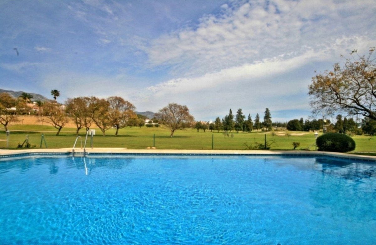 A bright blue swimming pool with a view of a lush green golf course and scattered trees under a cloudy sky.