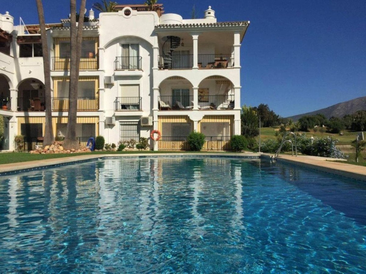 Apartment building with balconies overlooking a swimming pool and a scenic golf course view in the distance.