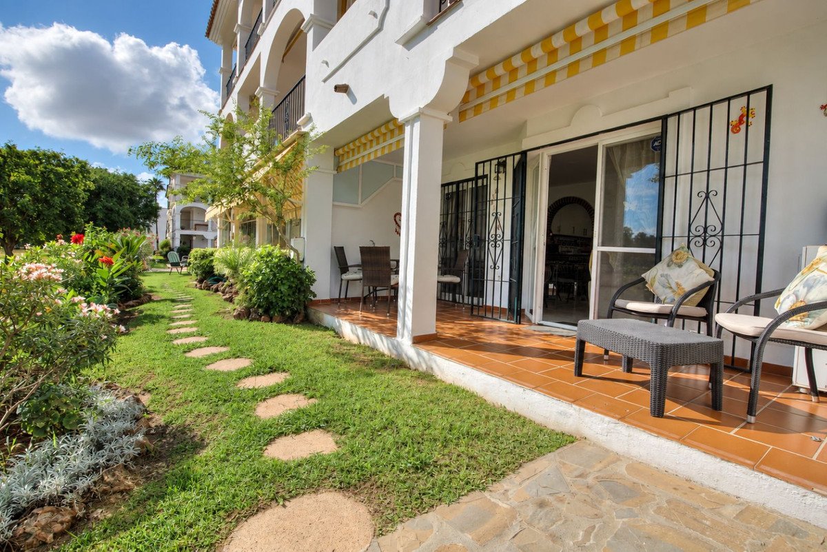 Terrace with outdoor seating overlooking a lush green garden with a paved pathway and blooming flowers.