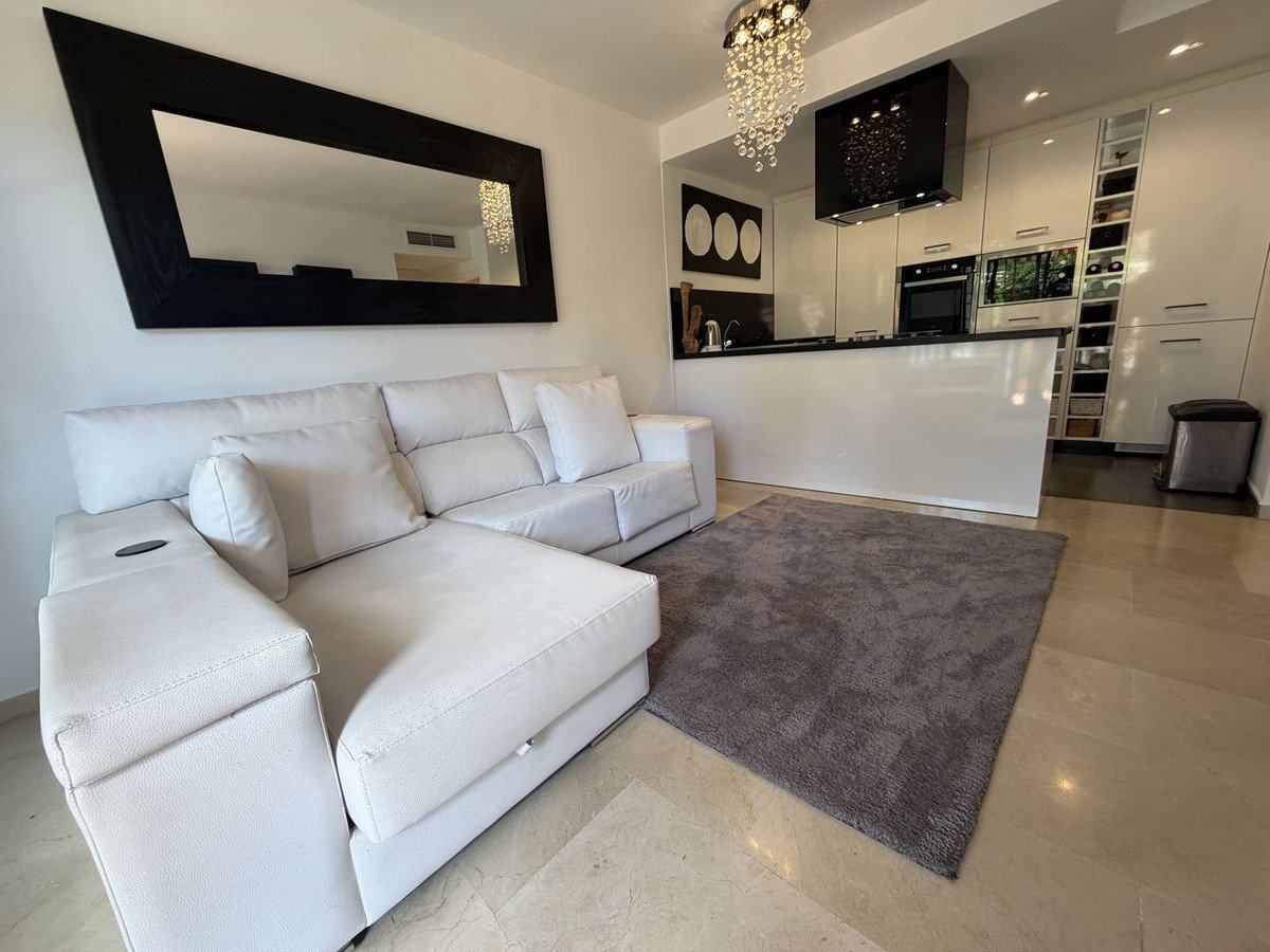 Modern living room featuring a white sectional sofa, gray rug, and sleek kitchen in the background