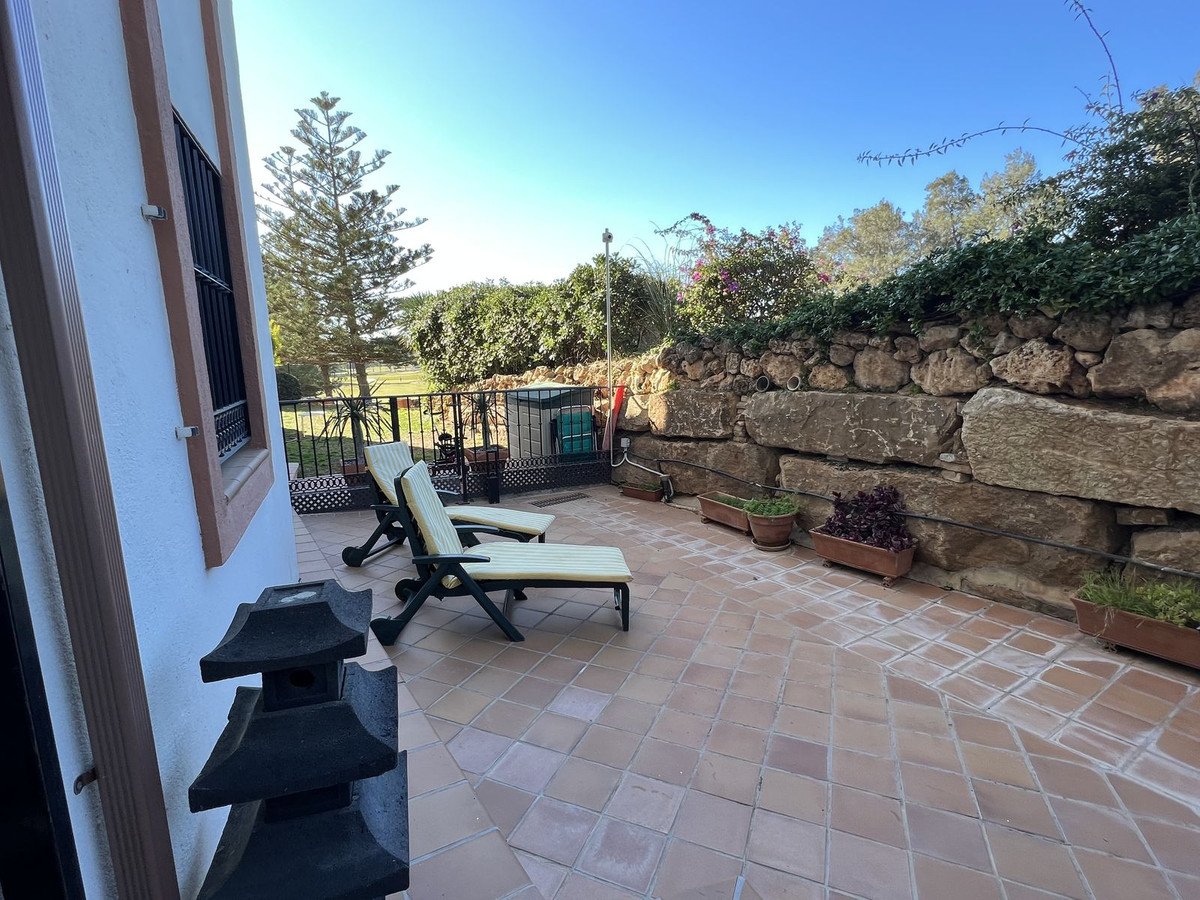 Terrace with lounge chairs, stone wall, and potted plants under clear blue sky