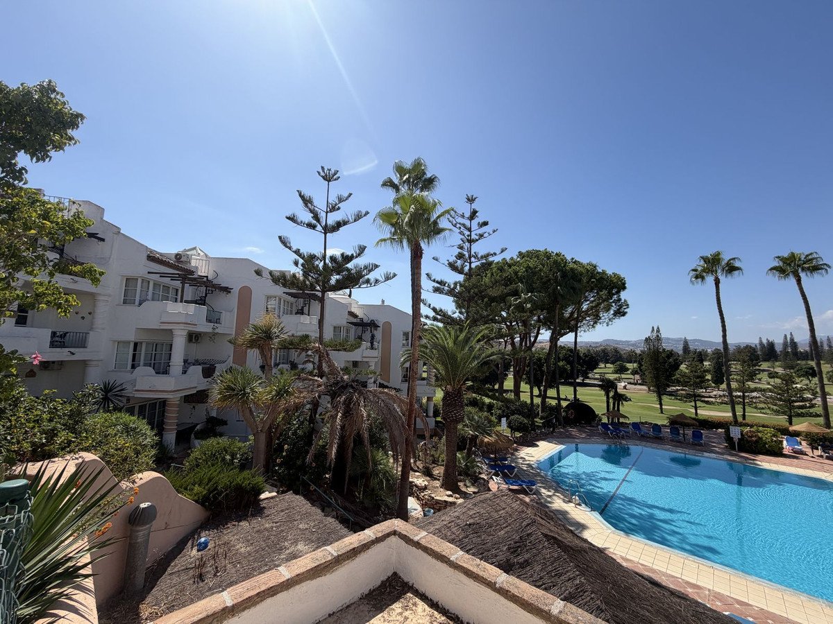 View of a resort property with a swimming pool and a golf course on a sunny day, featuring palm trees and a white building.