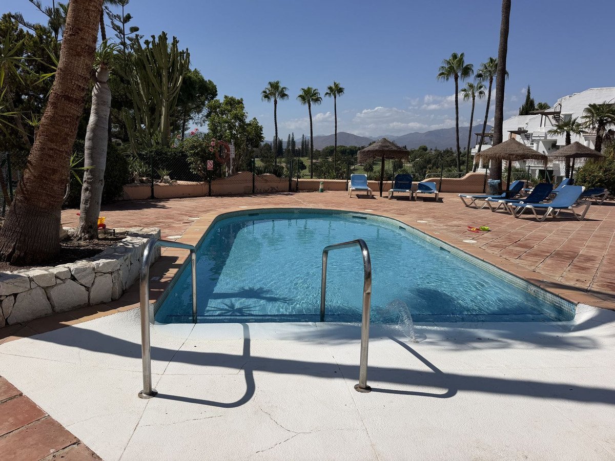 Outdoor swimming pool with blue lounge chairs, thatched umbrellas, and a mountain view.