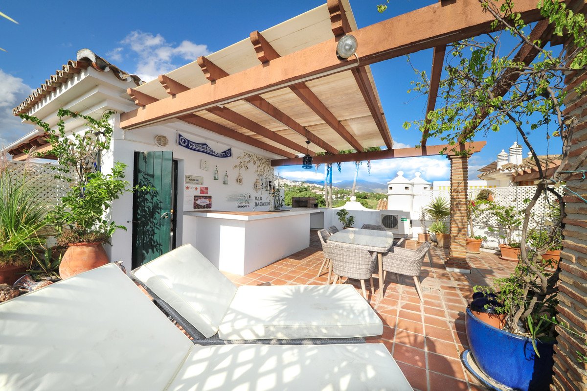 Rooftop terrace with outdoor bar, seating area, lounge chairs, and scenic mountain views under a wooden pergola.