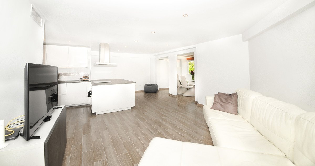Modern open-plan living area with a white sectional sofa, kitchen island, dining table, and TV.