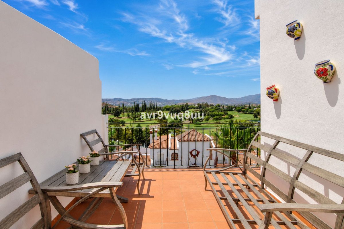 Terrace seating area with a view of a lush golf course and distant mountains under a blue sky.