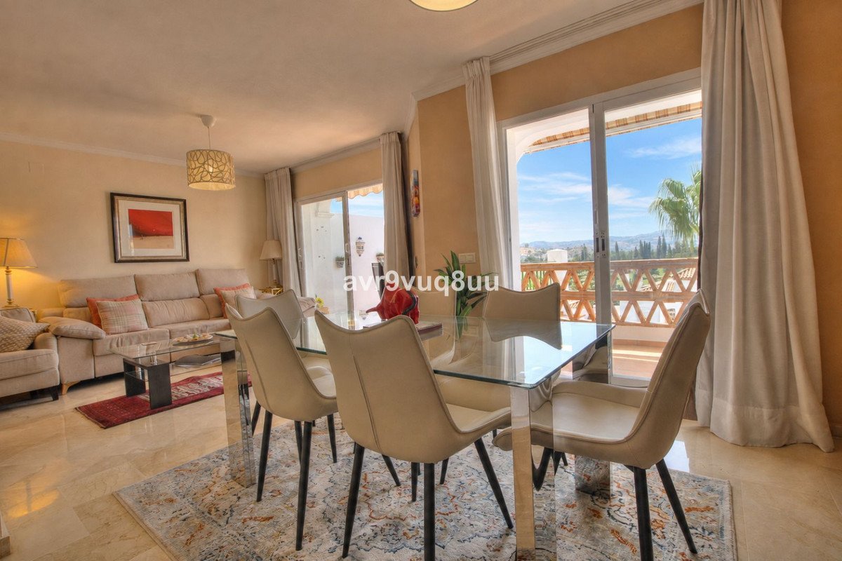 Modern dining room with glass table and chairs, leading to a balcony with mountain views.