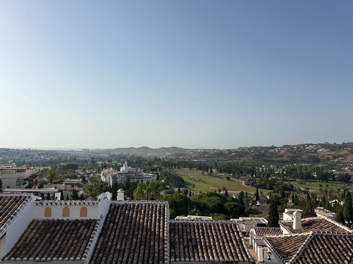 View from a rooftop terrace overlooking a golf course and distant hills on a clear day.