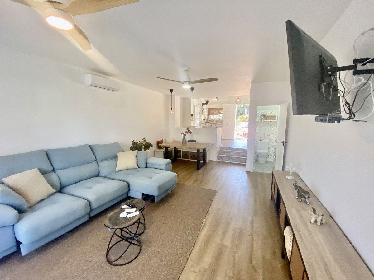 Modern living room with a large blue sectional sofa, coffee table, dining area, and a wall-mounted TV.