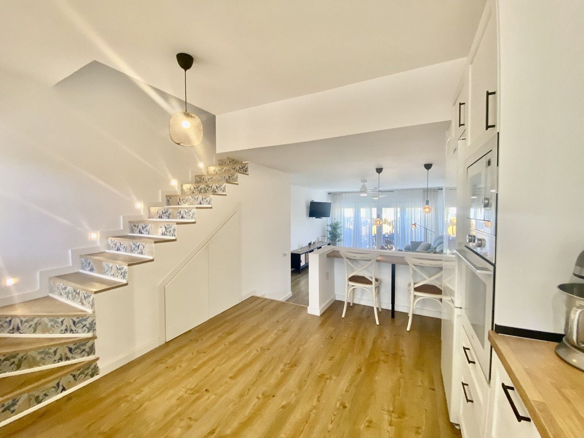 Modern interior showing a staircase with patterned risers, a kitchen island with stools, and a living room with large windows.